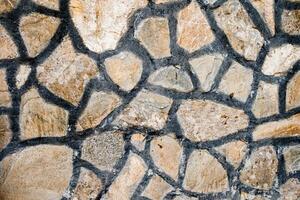 Close up of a stone wall with irregularly shaped stones and dark mortar lines, texture, background. photo
