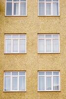 Facade of a yellow textured building with six white framed windows arranged in two columns and three rows. photo