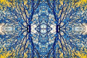 Symmetrical, kaleidoscopic image of tree branches with blue leaves against a yellow sky, creating an abstract and intricate pattern. photo