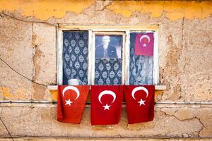 Window with Turkish flags hanging on and around it, set against an old, weathered yellow wall, in Turkey. photo