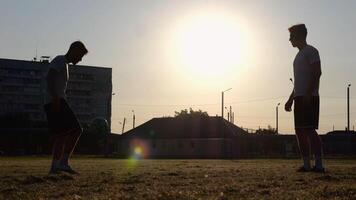 Silhouette of professional footballers kicking soccer ball with their heads on stadium at sunset. Two sportsmen showing tricks with ball while passing it to each other at field. Freestyle football photo