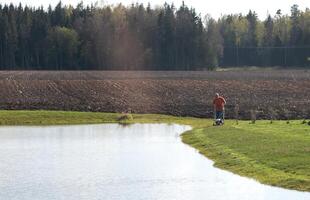 Photo of a middle-aged man mowing the grass at the pond during the beautiful spring evening.
