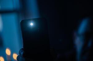 Male hand holds a smartphone with a burning flashlight with lighting window on the background photo