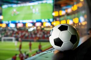 Soccer ball resting on rail with players competing on field in background photo