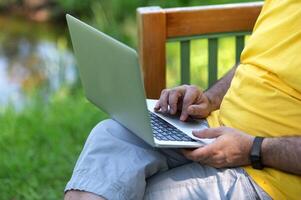 A man working and typing on laptop keyboard while sitting in the park, hand on laptop photo