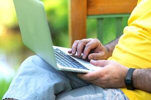 A man working and typing on laptop keyboard while sitting in the park, hand on laptop photo