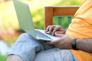 A man working and typing on laptop keyboard while sitting in the park, hand on laptop photo