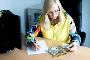 A middle-aged thoughtful woman counting euro money and takes notes at a desk in the home office photo