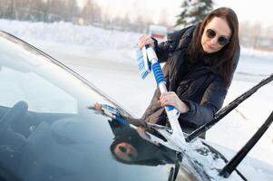 Woman cleans car with a brush from snow after a blizzar photo