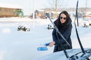 Woman cleans car with a brush from snow after a blizzar photo