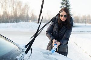 Woman cleans car with a brush from snow after a blizzar photo