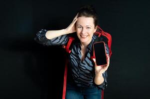 Smiling young woman with red backpack and smartphone isolated on black background photo