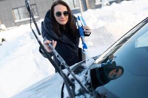 Woman cleans car with a brush from snow after a blizzar photo