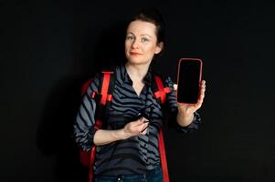 Smiling young woman with red backpack and smartphone isolated on black background photo