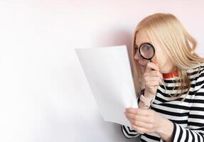Middle aged funny woman with magnifying glass reading document on gray wall background isolated photo