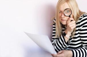 Middle aged funny woman with magnifying glass reading document on gray wall background isolated photo