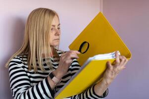 Middle aged funny woman with magnifying glass reading document on gray wall background isolated photo