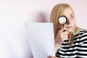 Middle aged funny woman with magnifying glass reading document on gray wall background isolated photo