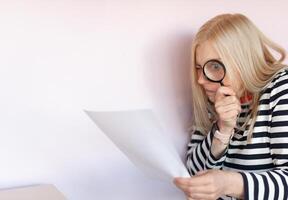 Middle aged funny woman with magnifying glass reading document on gray wall background isolated photo