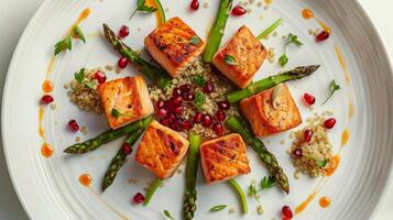Elegant dish of pan-seared salmon cubes over a bed of quinoa and asparagus, garnished with pomegranate seeds and a delicate sauce. photo