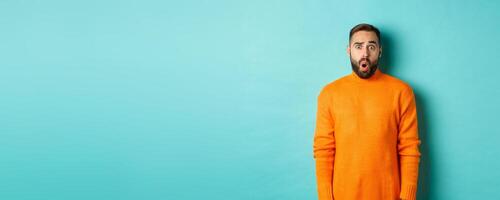 Shocked and confused man looking in awe at promo offer, standing near copy space on turquoise background photo