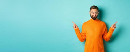 Doubtful and indecisive man pointing fingers sideways, showing different sides, two choices, looking skeptical, standing over light blue background photo