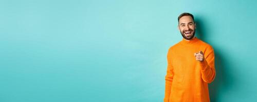 Handsome man laughing and pointing at camera, nodding in approval, agree with you, standing over light blue background photo