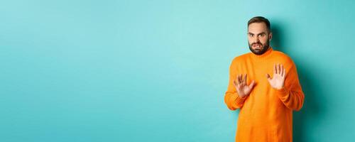 Alarmed guy shaking hands in rejection, declining and stepping away scared, standing over light blue background photo