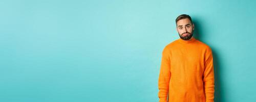 Sad man looking at camera, sulking and feeling distressed, standing over light blue background photo