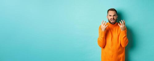 Image of angry man looking disappointed and mad, shaking hands and grimacing with disdain, standing distressed against light blue background photo