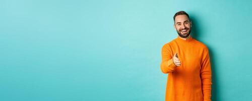 Friendly nice guy extend hand for handshake, greeting you and smiling, saying hello, standing over light blue background photo