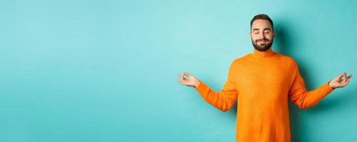 Image of relaxed and relieved man close eyes and smiling, feeling stress-free, meditating with calm expression, standing over light blue background photo