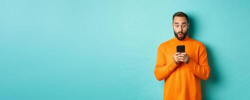 Image of man reading message with surprised face, standing amazed over light blue background photo