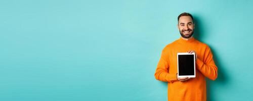 Technology. Smiling handsome man showing digital tablet screen, demonstrating application, standing over turquoise background photo