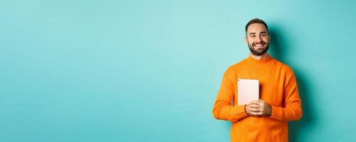 Handsome freelancer man holding laptop and smiling, standing happy over light blue background photo