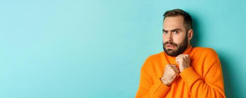 Close-up of scared bearded man looking startled and displeased, jumping from fear, standing over light blue background photo