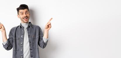 Cheerful smiling man pointing fingers sideways, showing left and right ways, looking happy at camera, standing on white background photo