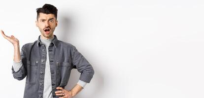 Confused and annoyed guy raising hand up and complaining, asking wtf happened, cant understand, standing on white background photo