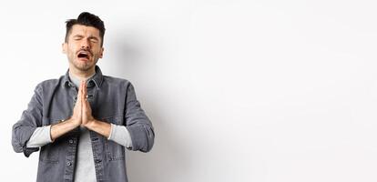 Miserable man begging for help, need something and crying, pleading with sad face, standing on white background desperate photo