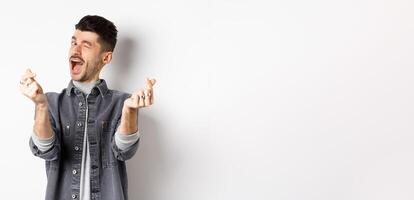Funny guy winking and showing hand hearts sign, feeling romantic and happy, standing on white background photo