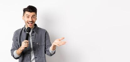Handsome smiling performer talking in mic, gesturing and performing, making speech with microphone, standing against white background photo