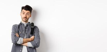Image of funny male entertainer or singer, holding microphone in pocket of jacket and look at camera with arms crossed, standing against white background photo