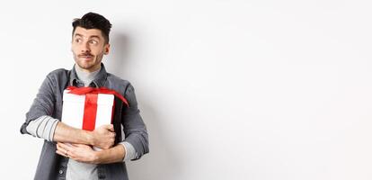 Excited man hugging romantic gift for girlfriend, waiting for valentines date with lover, looking at empty space logo with happy face, standing on white background photo