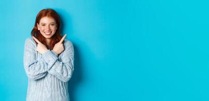 Cheerful redhead girl showing two choices, pointing sideways and smiling over blue background photo