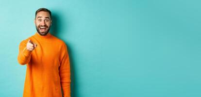 Surprised man stare happy and pointing at camera, recognize someone, excited about seeing something, standing over light blue background photo