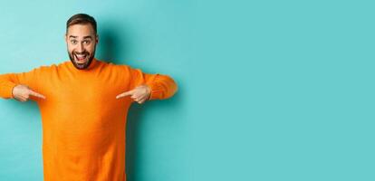 Happy man pointing at sweater, showing your logo banner on clothes, standing over light blue background photo