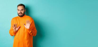 Alarmed guy shaking hands in rejection, declining and stepping away scared, standing over light blue background photo