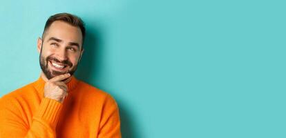 Close-up of caucasian male model having an idea, smiling and looking upper left corner thoughtful, imaging plan, standing over light blue background photo