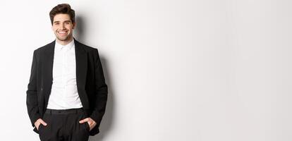 Image of handsome caucasian man in party suit, smiling pleased, attend formal event, standing over white background photo