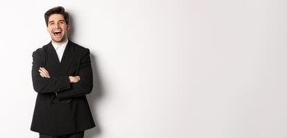Portrait of attractive adult man in suit laughing and looking happy, standing in suit with hands crossed over chest, posing against white background photo